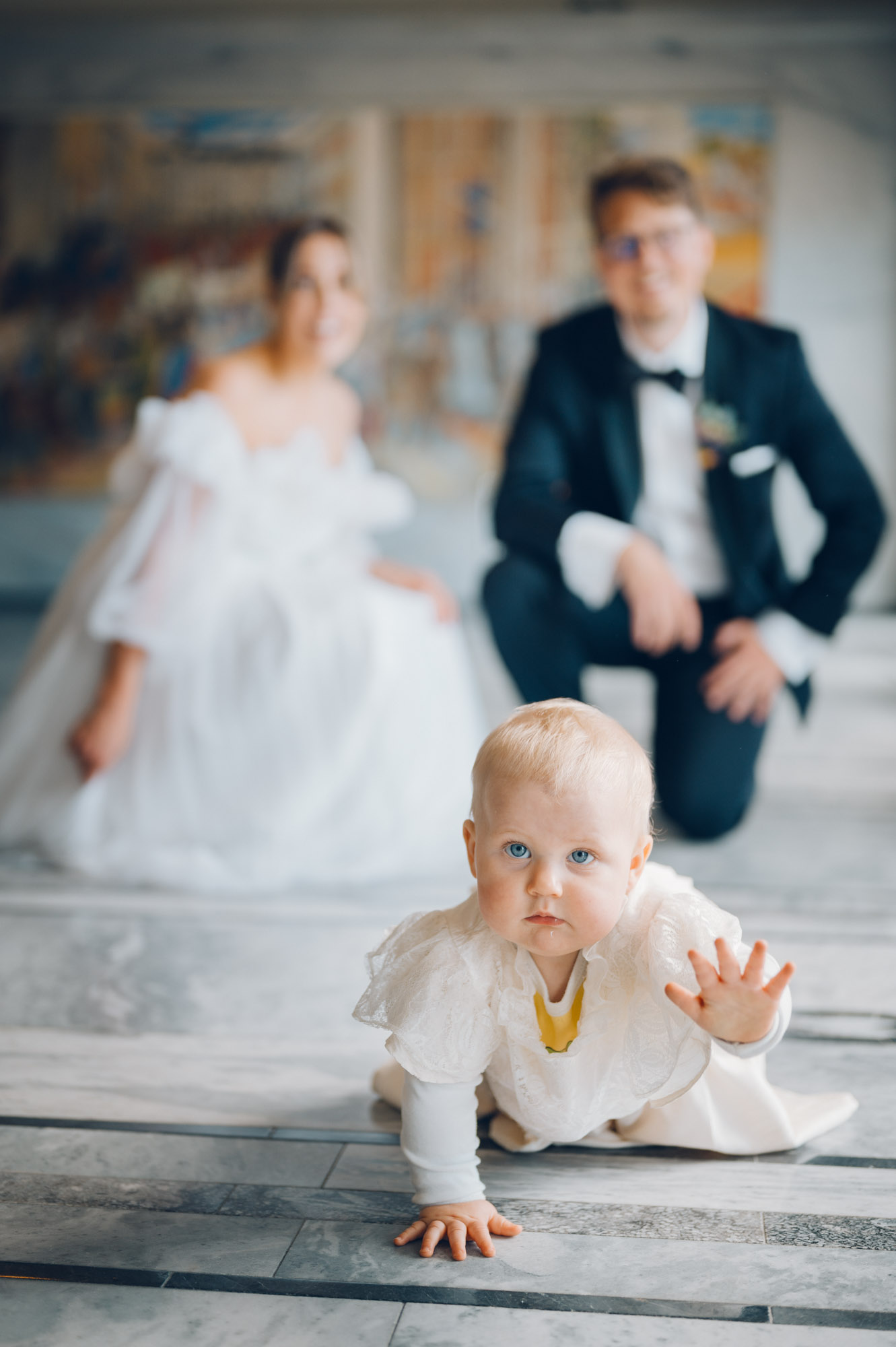 Et nydelig portrett av et brudepar med barnet sitt på Rådhuset. Barnet krabber mot kameraet, vi ser paret ute av fokus i bakgrunnen.