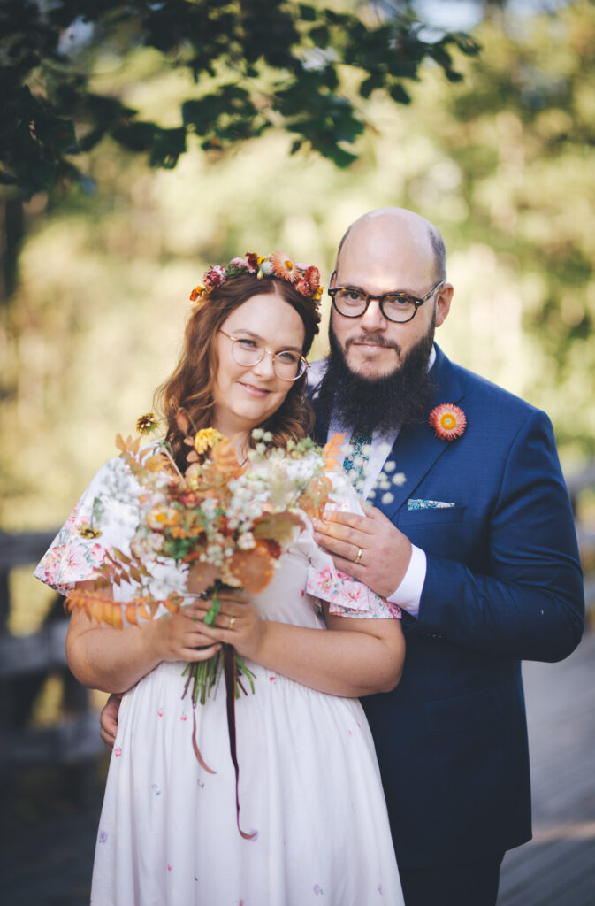 Bryllupsportrett med nydelige høstfarger. Bruden holder brudebuketten og brudgommen holder rundt bruden.