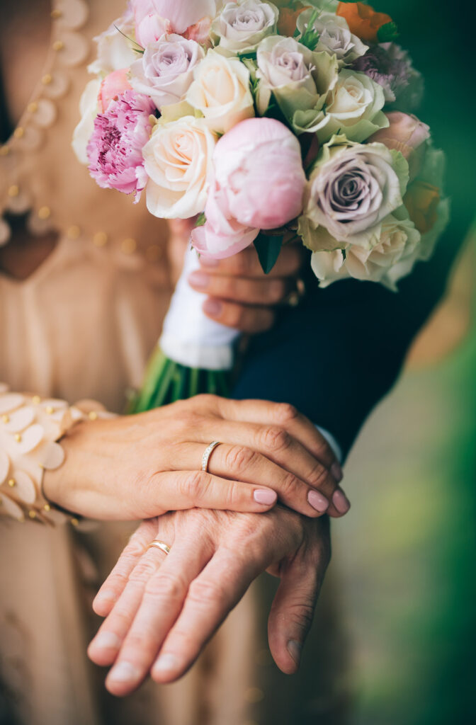 Nærbilde av ringene og brudebukett. Varme grønne og rosa farger
